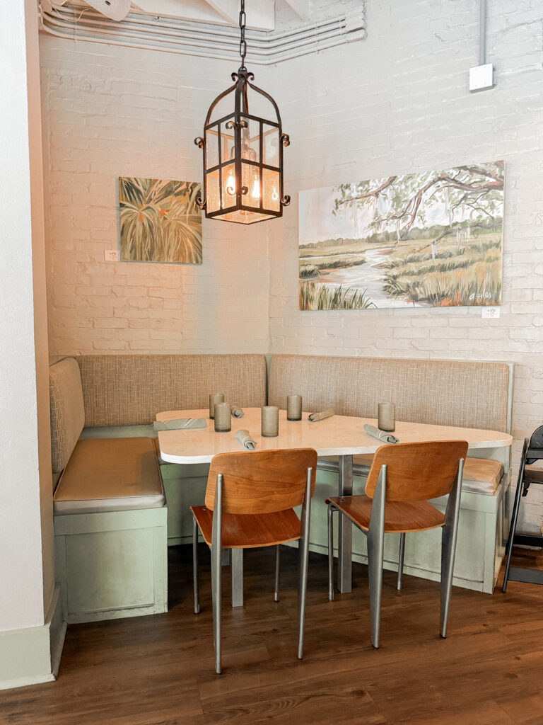 Dining area inside Ardsley Station, a popular restaurant in Savannah, Georgia, featuring booth seating, local artwork, white brick walls and a welcoming atmosphere.
