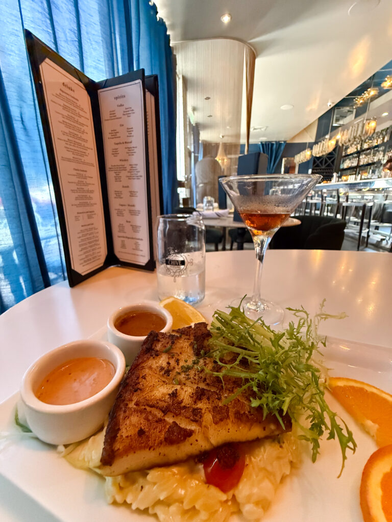 Pan-seared Chilean sea bass over creamy orzo at Chive Sea Bar & Lounge in Savannah, Georgia, served with house-made sauces and a cocktail.