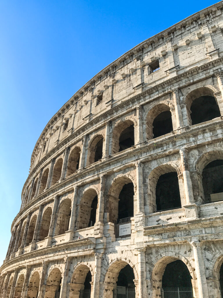 Close-up view of the ancient Colosseum in Rome, Italy, against a bright blue sky.