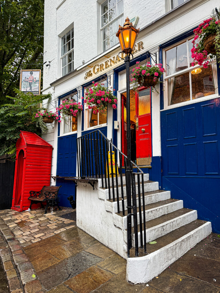 Exterior of The Grenadier pub in London, England, featuring colorful flower baskets and its iconic red sentry box.