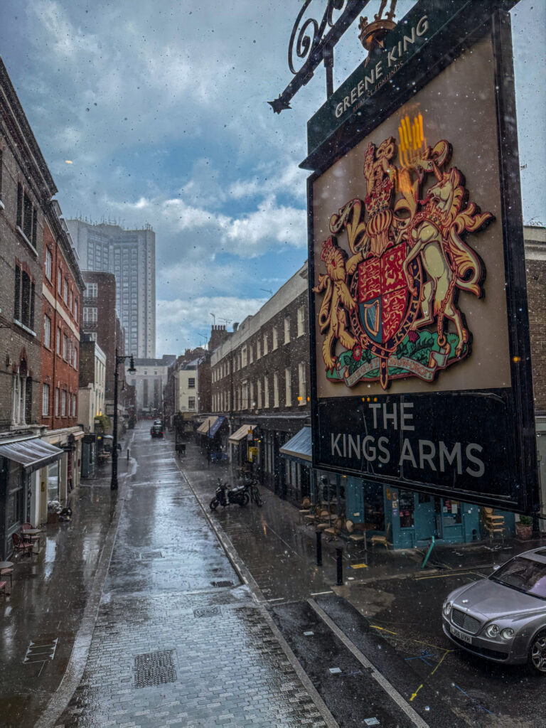 Rainy street view from a traditional London pub overlooking a quiet city street during a summer rainstorm.